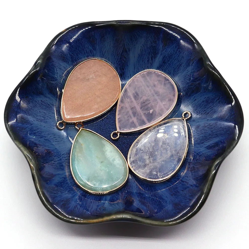 A dark blue ceramic dish holds three oval gemstone pendants, including rose quartz and agate.