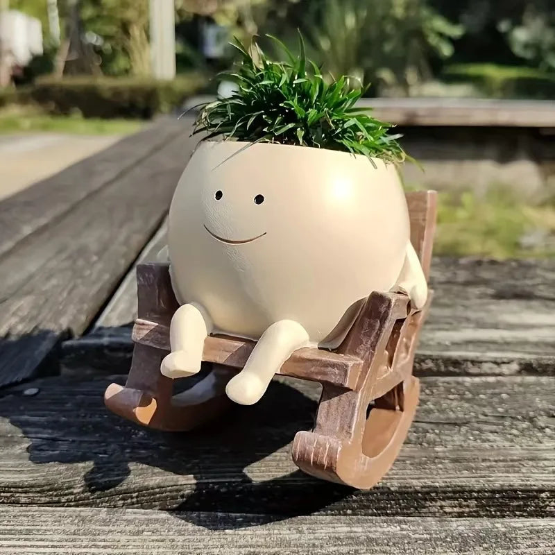 A beige resin ornament shaped like a smiling face, potted with green foliage, rests on a wooden surface.