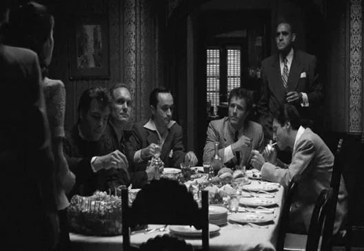 Scène en noir et blanc du film Scarface avec plusieurs hommes assis à une table.
