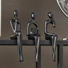 Three black abstract thinker sculptures in a row on a dark shelf.