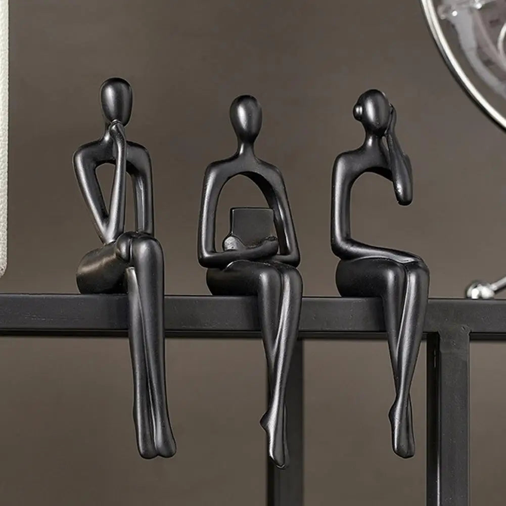 Three black abstract thinker sculptures in a row on a dark shelf.