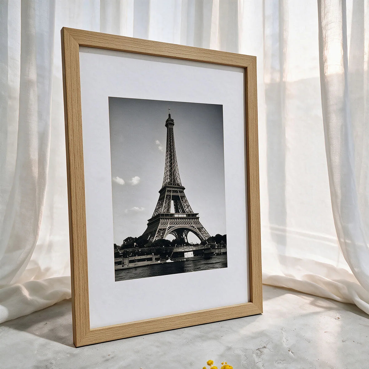 A framed black and white photograph of the Eiffel Tower in a light wood frame.