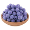 A pile of purple glitter resin beads for jewelry making in a wooden bowl.