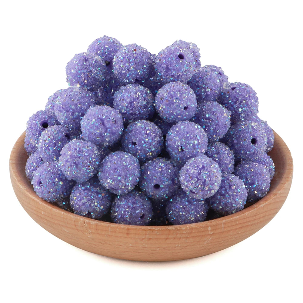 A pile of purple glitter resin beads for jewelry making in a wooden bowl.