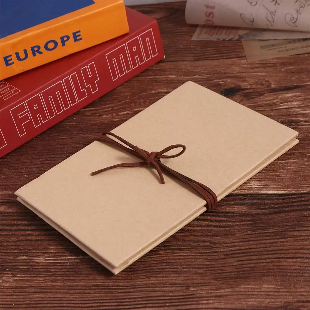 A handcrafted accordion photo album with a light beige cover and brown twine tied on top, resting on a wooden surface next to