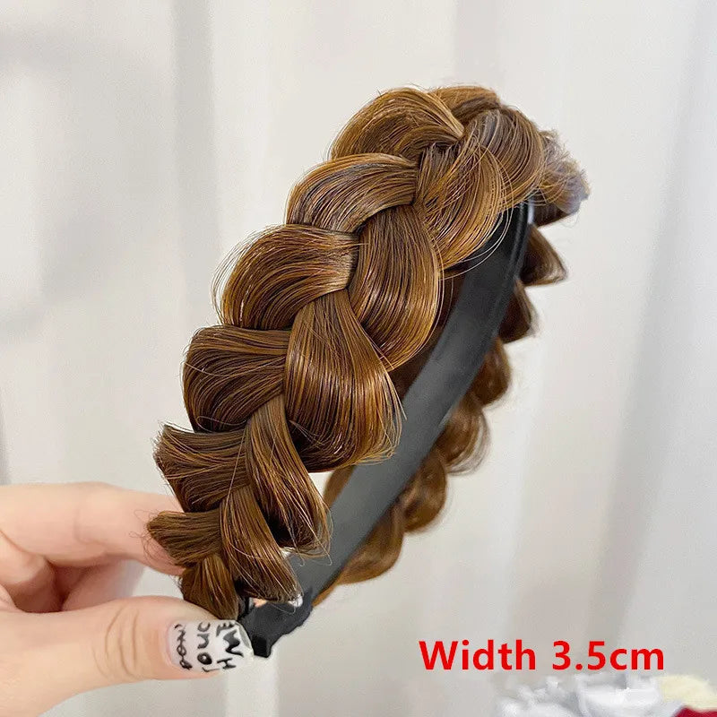 A hand holds a braided hairstyle featuring warm brown hair styled in a thick braid on a black hair clip.