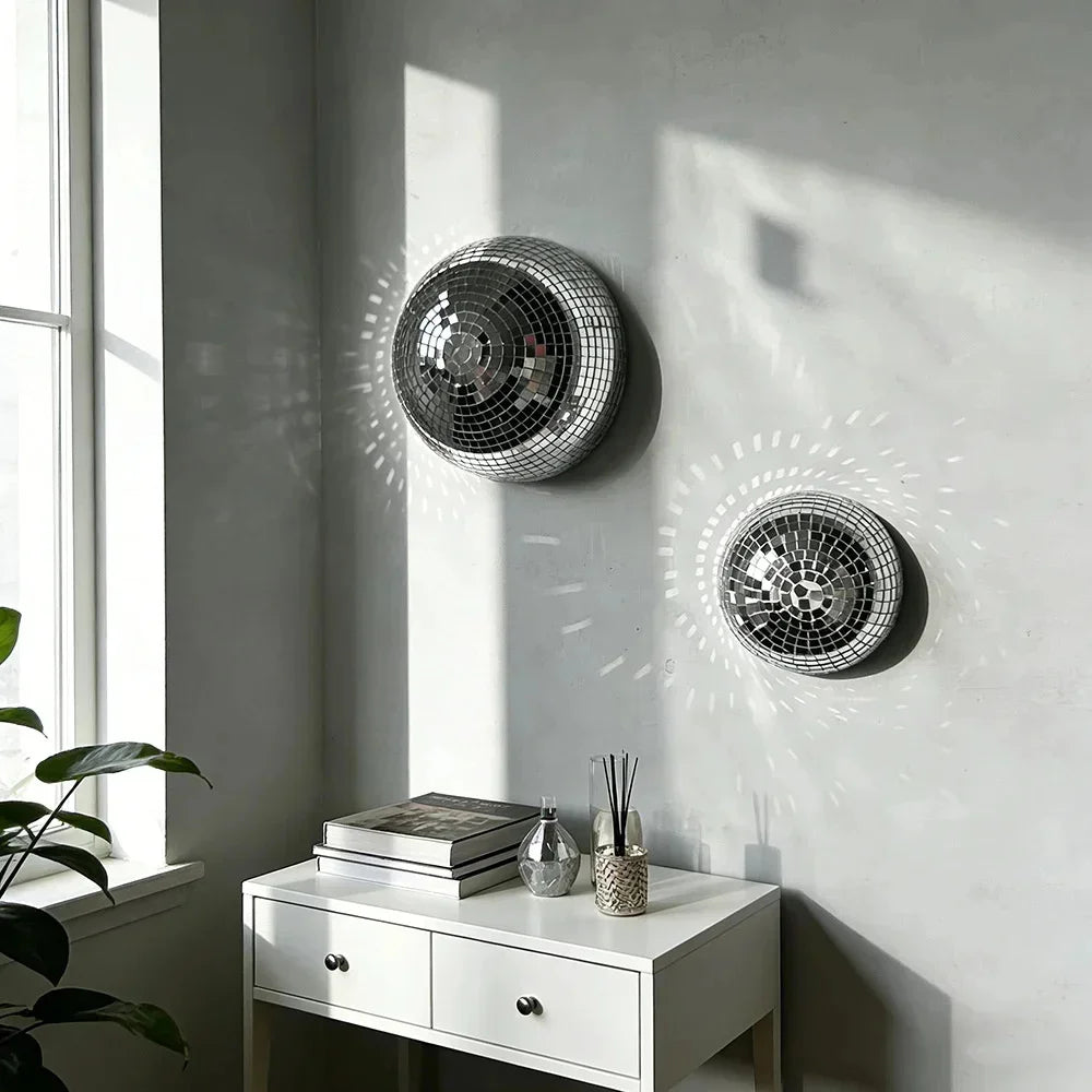 Boule disco en verre miroir argenté, décoration murale accrochée à un mur gris clair près d'une fenêtre.