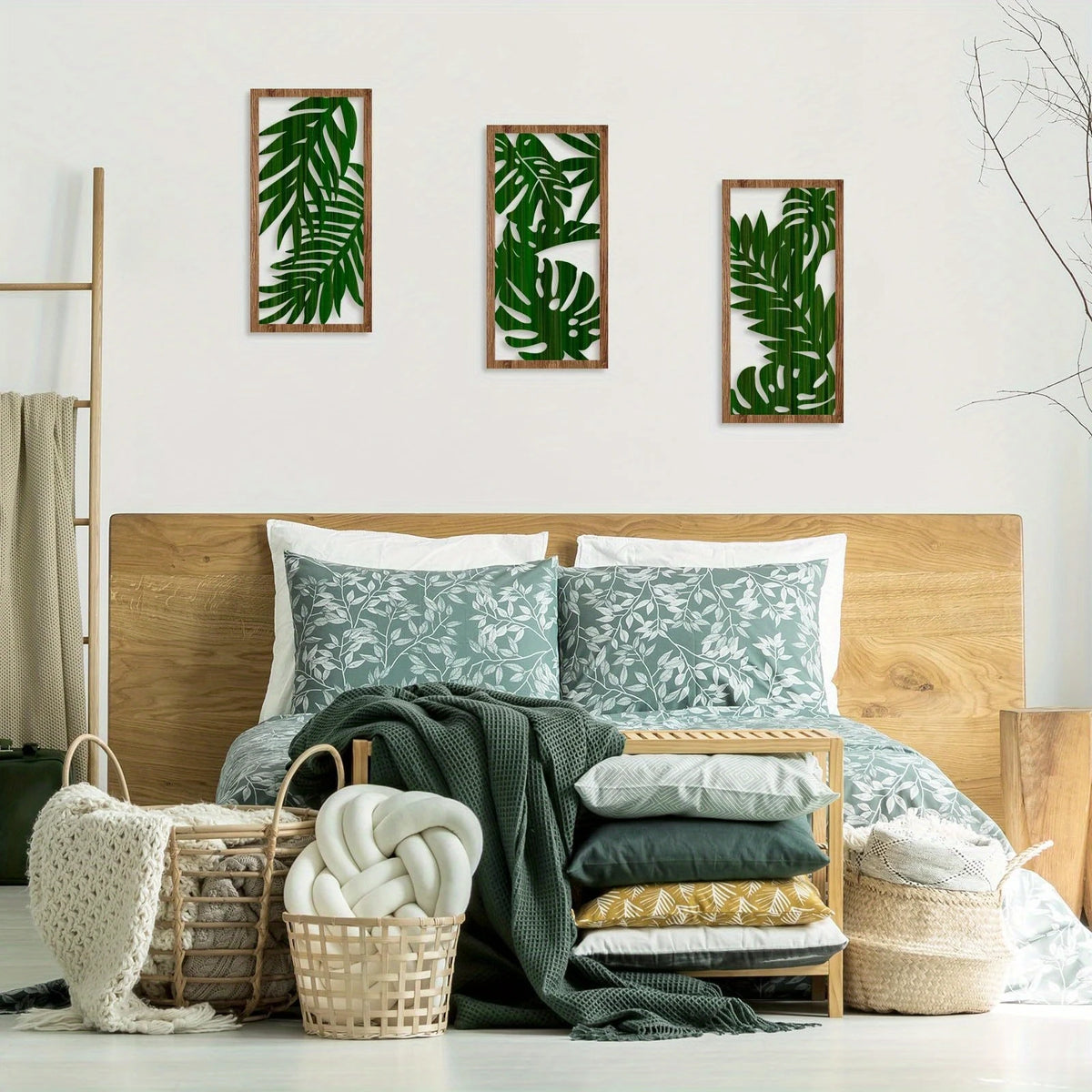 A set of three framed green leaf botanical prints displayed on a white wall above a wooden bed.