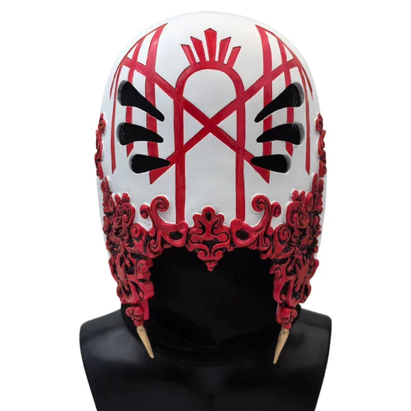 A white mask with red markings resembling a stylized crown or helmet, displayed on a black mannequin.