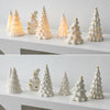 A collection of ceramic glow-in-the-dark mini Christmas tree decor in white and yellow shades arranged on a white surface.