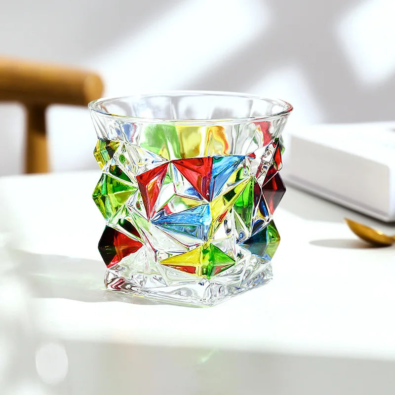 Faceted crystal whiskey glass with multicolored geometric facets resting on a white surface.