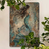 Vintage mermaid metal wall art sign featuring a woman with long flowing hair and a teal scale tail against an aged background