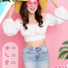 A woman models pink rimless heart sunglasses with a straw hat and a white cropped top and denim skirt.