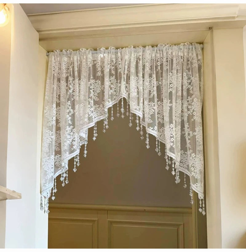 A sheer white beaded lace valance curtain with a scalloped edge hangs in a recessed doorway.