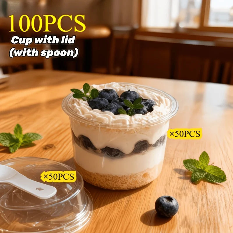 A clear plastic cup filled with a creamy dessert topped with blueberries and mint leaves, displayed on a wooden table.