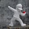A white resin sculpture of a figure throwing a red ball against a dark, textured background.