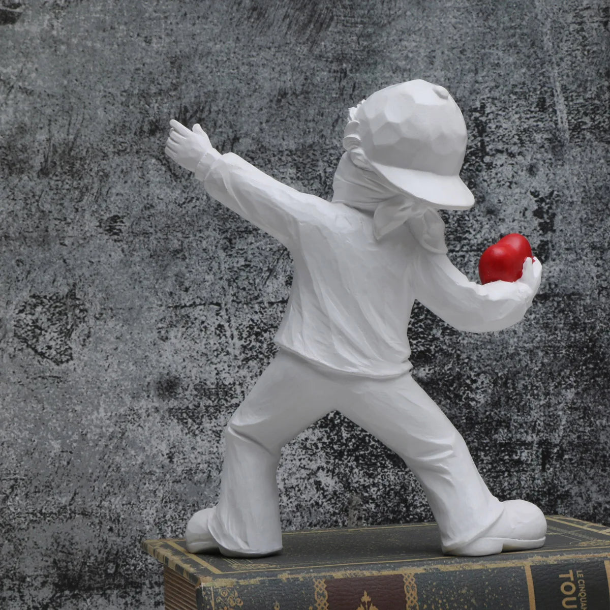 A white resin sculpture of a figure throwing a red ball against a dark, textured background.