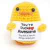A yellow crochet duck doll with black eyes and an inspirational card attached.