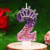 Glitter number 2 birthday candle with a rhinestone crown cake topper on a wooden surface.