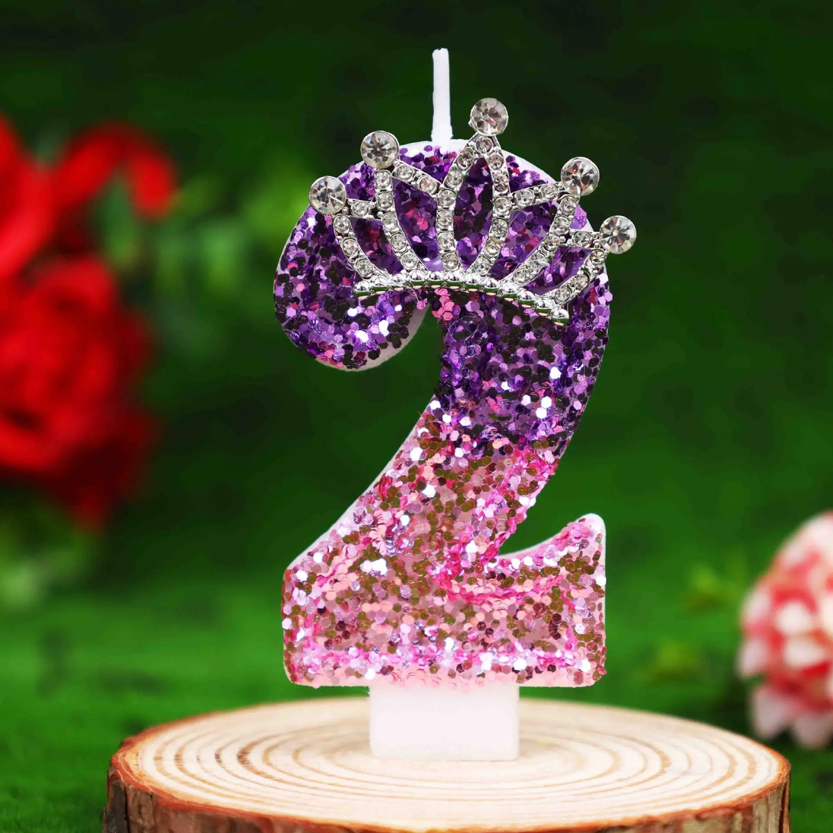 Glitter number 2 birthday candle with a rhinestone crown cake topper on a wooden surface.