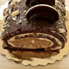 A dark chocolate layer cake with frosting and chocolate decorations displayed on a gold disposable plate.