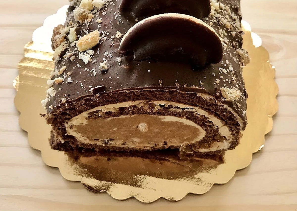 A dark chocolate layer cake with frosting and chocolate decorations displayed on a gold disposable plate.