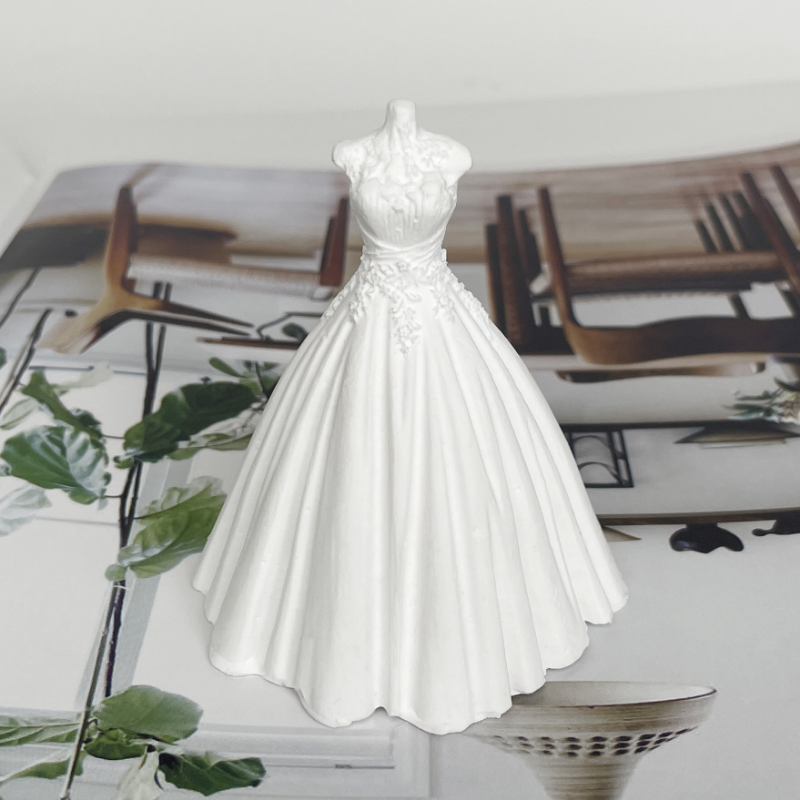 A white silicone mold of a wedding dress is displayed on a surface next to greenery.