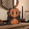 An orange carved pumpkin decoration set displayed on a wooden surface next to a framed mirror and a black candle.