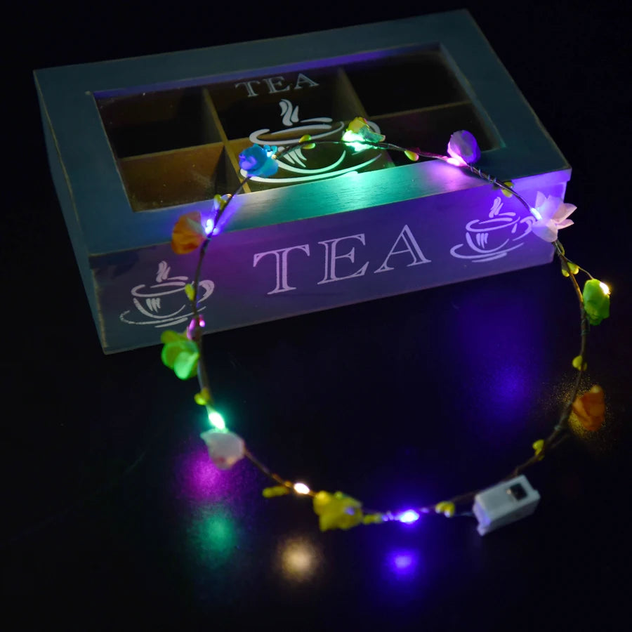 A glowing flower wreath headband with ten LEDs rests on a teal box featuring the word TEA.