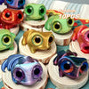 A collection of 10 3D printed frog car ornaments featuring various colors and color-shifting eyes displayed on wooden stands.