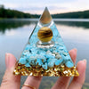 Handmade resin orgonite pyramid with natural obsidian and copper coil resting on a hand.