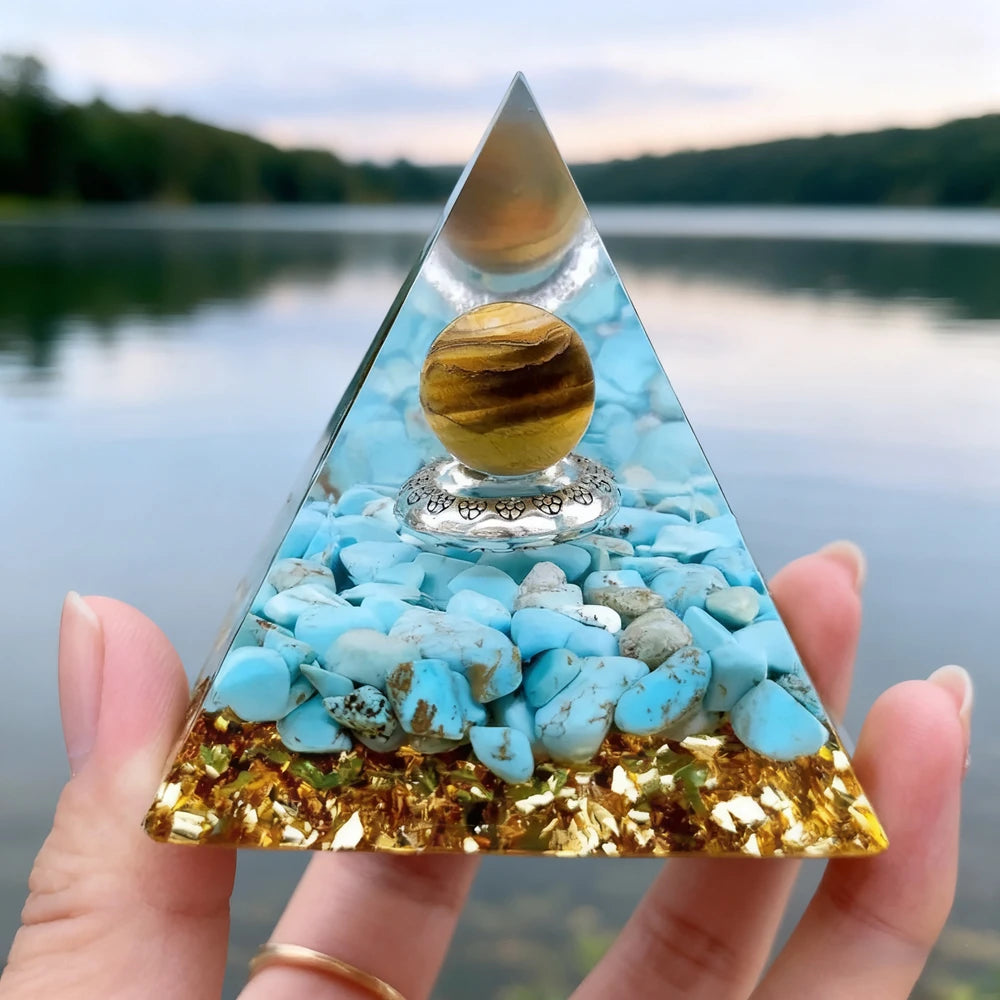 Handmade resin orgonite pyramid with natural obsidian and copper coil resting on a hand.