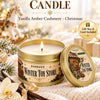 A golden candle in a tin is shown with a gift box and card, set against a snowy Christmas background.