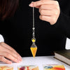 A hand holds a silver crystal necklace with a yellow pendant against a black background.