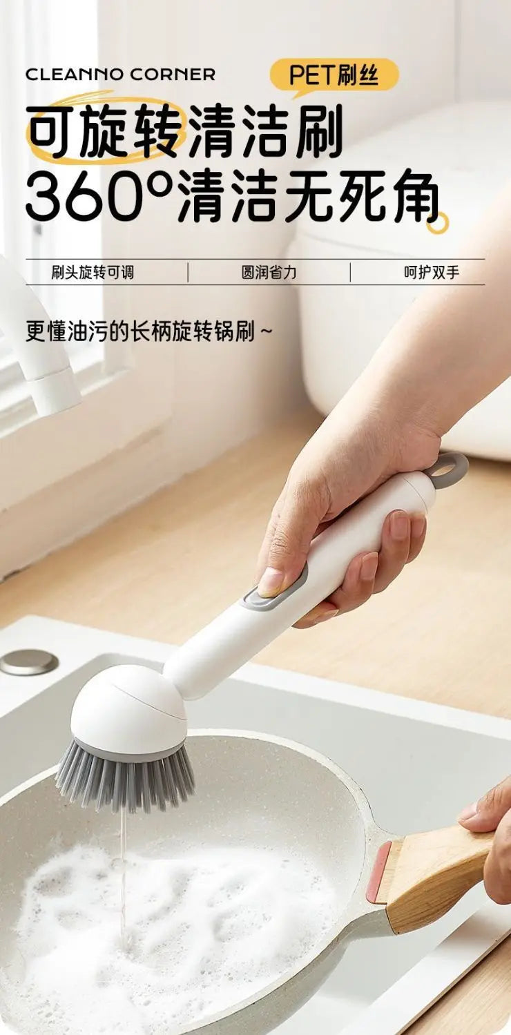A hand is using an adjustable long-handled liquid washing brush to clean a frying pan with soap in a kitchen setting.