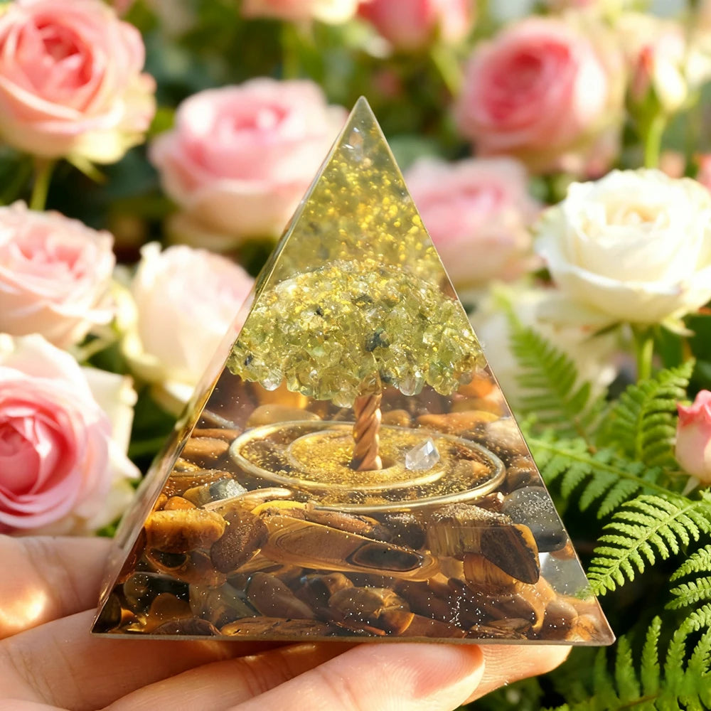 Handmade resin orgonite pyramid with natural obsidian and copper coil resting on green foliage