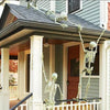 A white skeleton decoration is hanging from the eaves of a house with green siding and a dark roof.