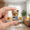 A hand holds a sparkling Yorkshire Terrier acrylic pendant necklace against a blurred indoor background.