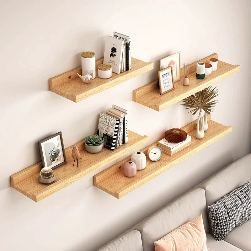 A set of natural wood floating shelves mounted on a wall displaying various decorative items like books and small plants.