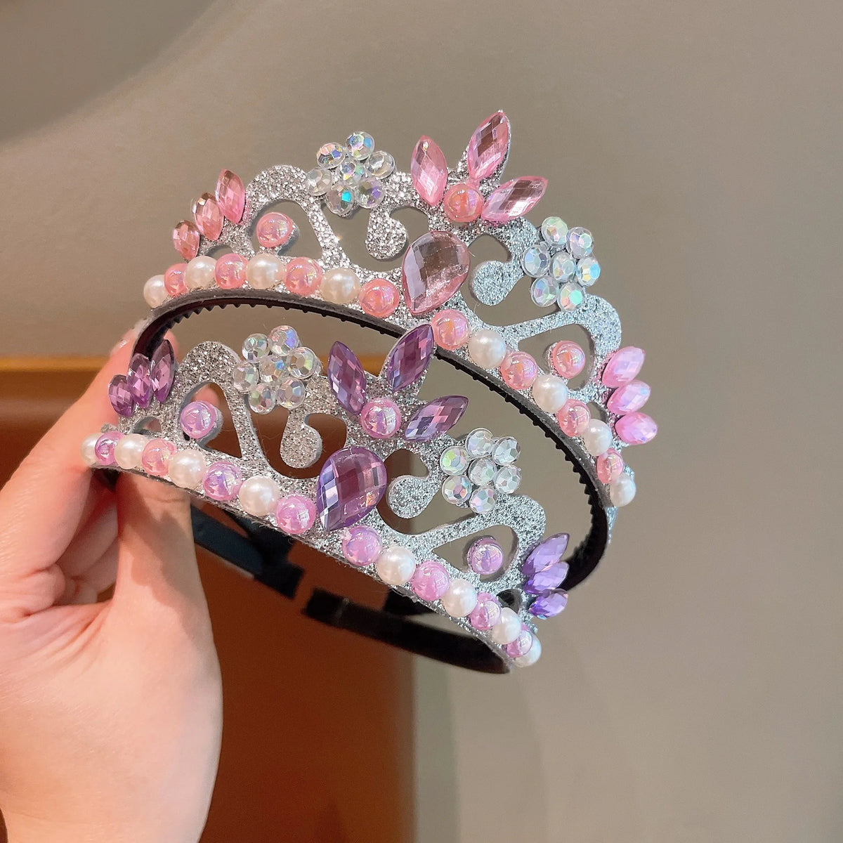 A hand holds a set of three sparkling pearl and floral headbands for girls and women.