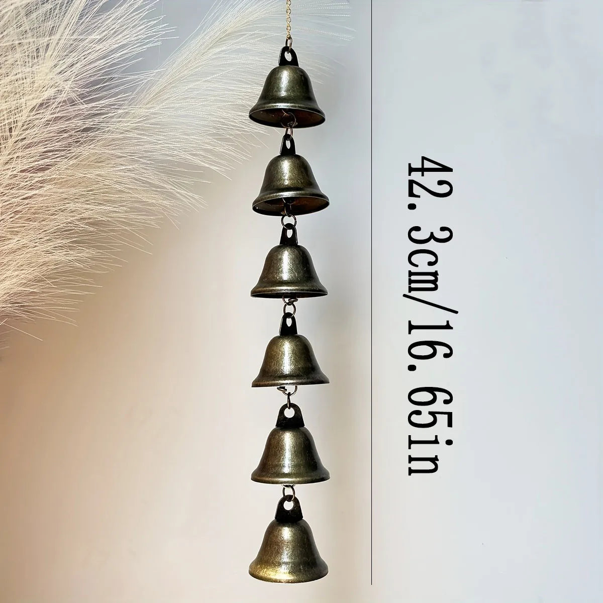 A vertical arrangement of bronze metal wind chimes hanging from a thin cord against a white background.