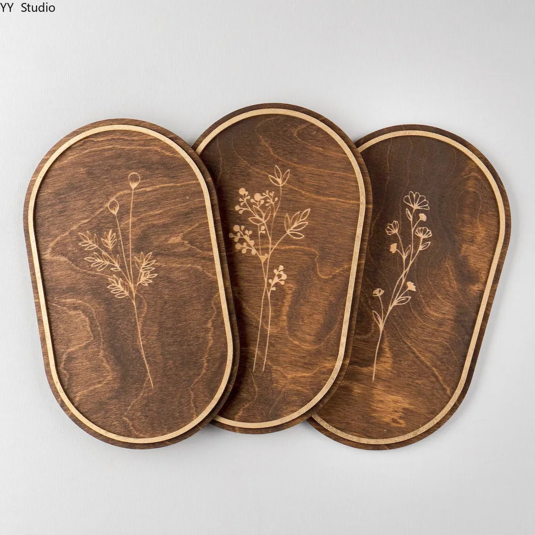 A set of three oval wooden wall decor pieces featuring delicate botanical engravings on dark wood.