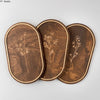 A set of three oval wooden wall decor pieces featuring delicate botanical engravings on dark brown wood.