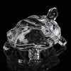 Clear glass miniature tortoise statue reflecting on a dark surface.