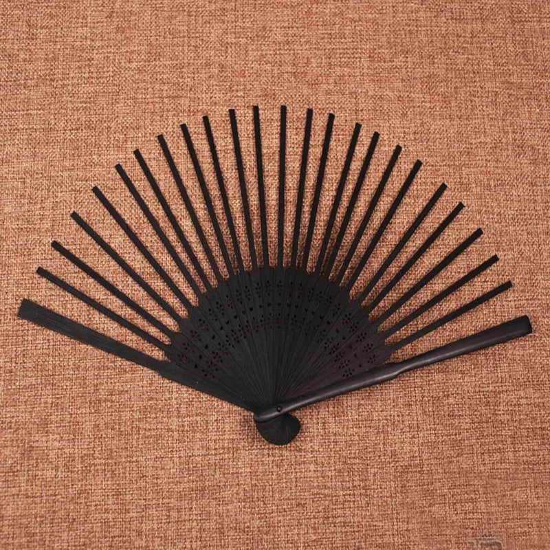 Un éventail main squelette en bambou pliante noir, présenté sur un fond marron texturé.
