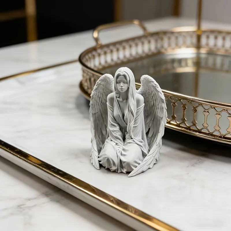 Estatua de ángel plateada con alas sobre una superficie de mármol junto a una bandeja con borde dorado.