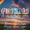 Retro metal sign with the text FOLLOW THAT DREAM displayed against a sunset sky.