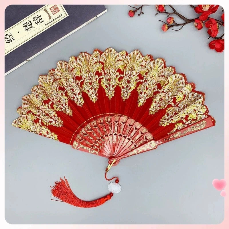 A red and gold folding fan with intricate traditional Chinese designs, displayed against a gray background.