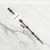 A long, slender metal wand replica with a textured handle and a metal core, shown against a white marble background.