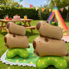 Several tan foil balloon shaped like capybaras are displayed outdoors on a green blanket.